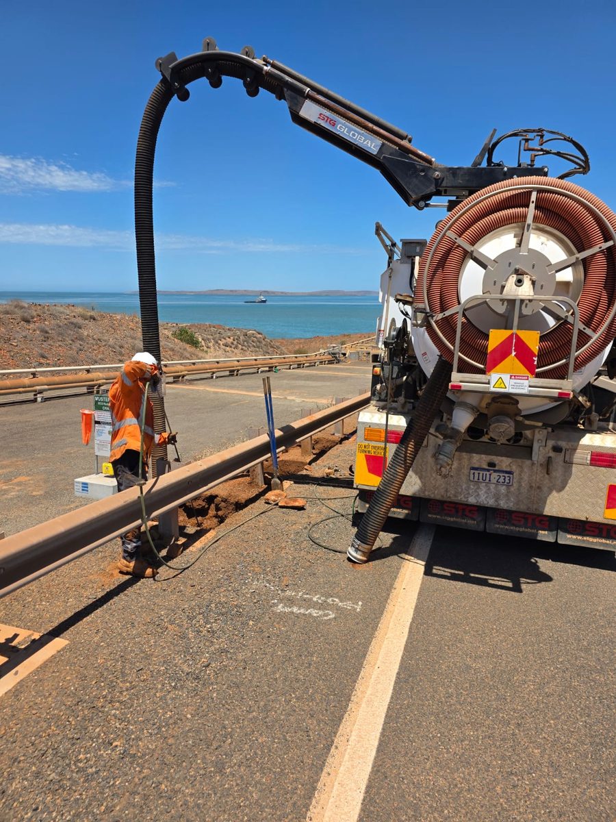 Vac truck boom potholing guardrail posts on a coastal highway